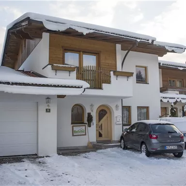 A modern house in the snow with wooden cladding. Cars are parked in front of the house and the surroundings are wintry.