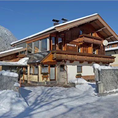 A beautiful wooden house in winter with snow-covered terrain. The sky is clear and blue.