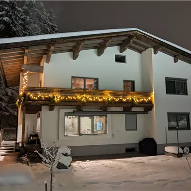 A modern house in the snow, illuminated with lights. The surroundings are wintry and peaceful.