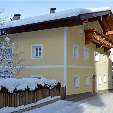 A pretty yellow house in a snowy landscape. The road is quiet and lined with snow-covered trees.