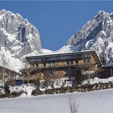 Ein malerisches Bergdorf im Schnee, umgeben von beeindruckenden Felsen. Die Gebäude haben eine gemütliche alpine Architektur.