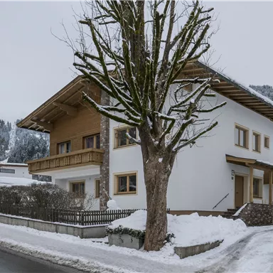 A modern house in a winter landscape, surrounded by snow. Trees and mountains are visible in the background.