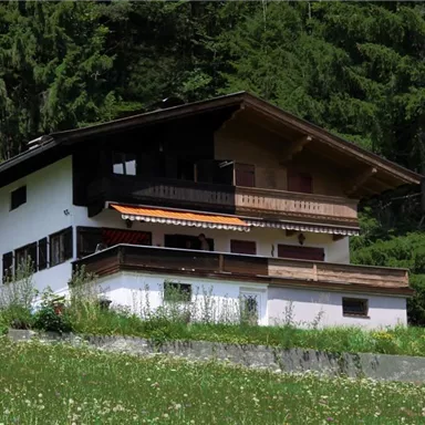 A picturesque house in the mountains, surrounded by green meadows and trees. The balcony offers a beautiful view of nature.