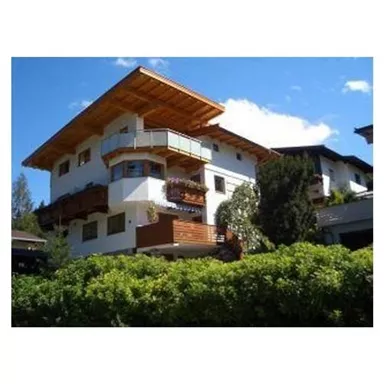 A modern house with a wooden balcony and a green garden. The sky is clear and blue.