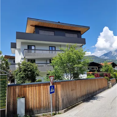 Ein modernes Haus mit mehreren Etagen und einer Dachterrasse. Umgeben von Bäumen und einem gepflegten Garten in einer ruhigen Straße.