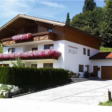 A charming holiday home with balconies full of flowers. The surroundings are green and surrounded by trees.