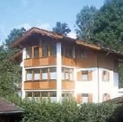 Ein österreichisches Haus mit Holzverkleidung und großen Fenstern. Umgeben von grünem Garten und Bäumen.