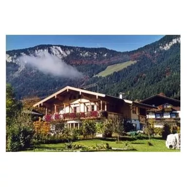 Ein traditionelles Alpenhaus umgeben von grünen Wiesen und Bergen. Die Landschaft ist malerisch und neblig in der Ferne.