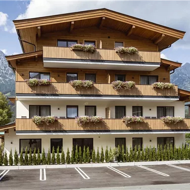 A modern building with wooden elements and flower boxes. In the background, impressive mountains are visible.