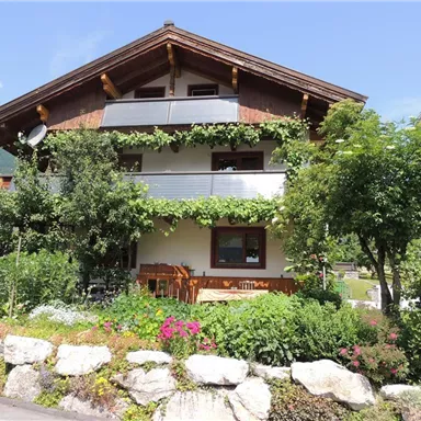 A friendly house with a beautiful garden and blooming plants. The surroundings are green and stretch beneath a clear sky.