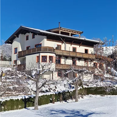 Ein modernes zweistöckiges Haus in einem verschneiten Landschaft. Im Hintergrund ist ein klarer blauer Himmel zu sehen.