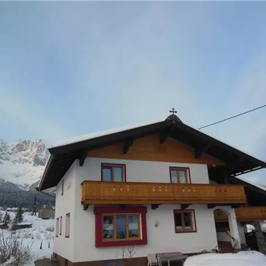 A charming house in the snow with a balcony and mountain view. The sky is clear and the surroundings are wintry.