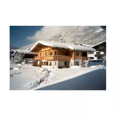 Ein gemütliches Holzhaus im Schnee, umgeben von schneebedeckten Bergen. Der Himmel ist klar und blau.