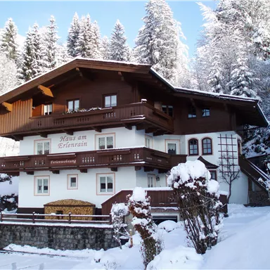 Ein charmantes Holzhaus im Schnee, umgeben von hohen, verschneiten Bäumen. Die Atmosphäre ist gemütlich und winterlich.