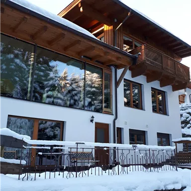A modern house with wooden details, surrounded by snow. The windows reflect the trees in the background.
