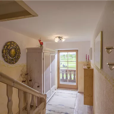 Ein heller Flur mit einem Holzgeländer und einem Fenster, das auf einen Gartenblick zeigt. Die Wände sind in sanften Farben gehalten und mit dekorativen Elementen verziert.