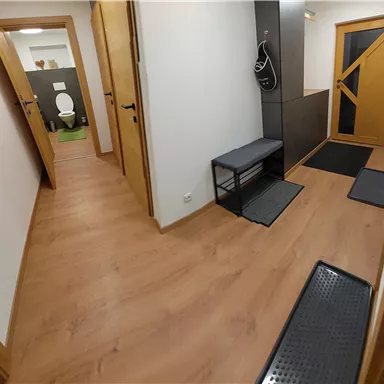 Ein heller Flur mit einem Holzboden und verschiedenen Türen. An der Wand hängt ein Bild von einer Waldlandschaft.
