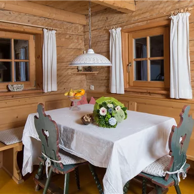 A cozy dining area in a wooden apartment. The table is decorated with a white tablecloth and a bouquet of flowers.