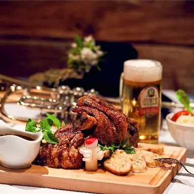 A delicious dish with perfectly roasted meat on a wooden board. Served with beer, sauce, bread, and fresh sides.