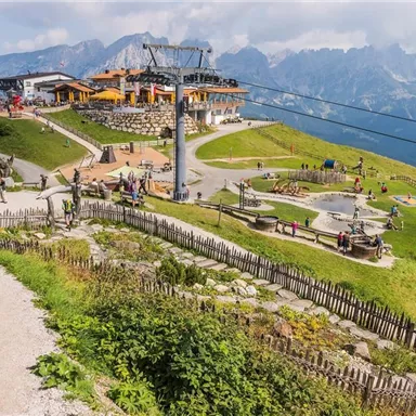 Ein malerischer Bergort mit vielen Besuchern. Im Hintergrund sind beeindruckende Berge und eine Seilbahn zu sehen.