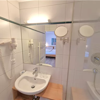 A modern bathroom with a sink and a large mirror. The walls are brightly tiled and there is a hairdryer.