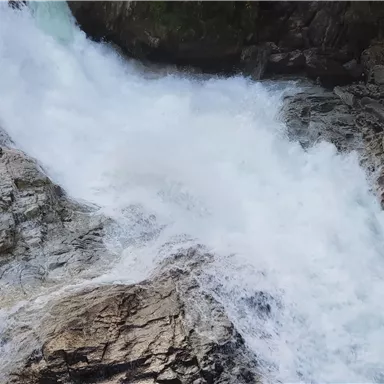 Ein wilder Wasserfall fließt über steinige Felsen. Das Wasser sprudelt und erzeugt eine lebendige, spritzige Atmosphäre.