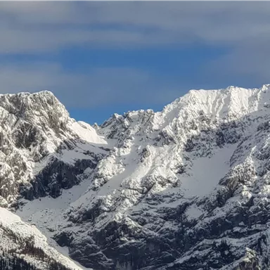 Eine beeindruckende Berglandschaft mit schneebedeckten Gipfeln und einem klaren blauen Himmel. Die Felsen sind steil und majestätisch.
