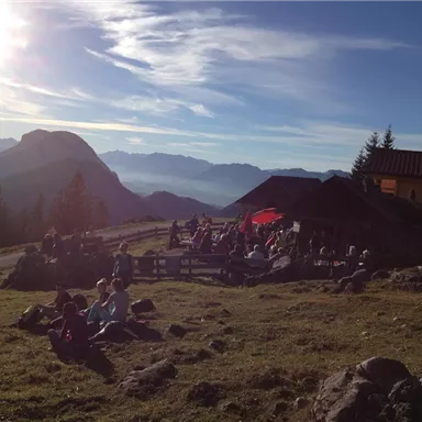 A picturesque mountain landscape with people relaxing outdoors. In the background, there are mountains and a clear sky.