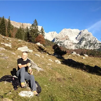 A man is sitting in a mountainous landscape and enjoying nature. In the background, there are high mountains and a blue sky.