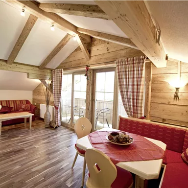 Ein gemütlicher Wohnraum mit Holzdecke und eleganten Möbeln. Es gibt einen Essbereich und große Fenster, die für viel Licht sorgen.