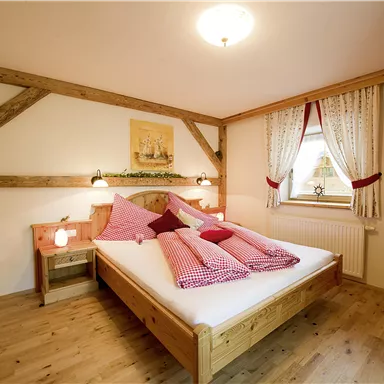 Ein gemütliches Schlafzimmer mit einem Holzbett und dekorativen Kissen. Die warmen Farben und Holzelemente schaffen eine einladende Atmosphäre.