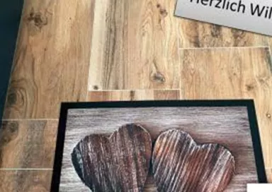 A welcoming doormat with two wooden hearts. Above it, there is a sign that says "Warm Welcome".
