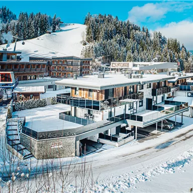 A modern hotel building in a snowy landscape. Surrounded by snow-covered mountains and a clear blue sky.