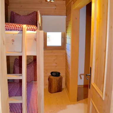 A cozy room with a loft bed and red checkered cushions. The room has wooden walls and a warm, inviting character.