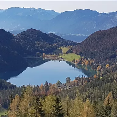 Ein malerischer See umgeben von Bergen und Wäldern. Die bunte Herbstlandschaft spiegelt sich im klaren Wasser des Sees.