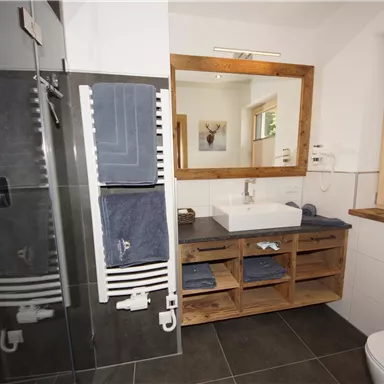 A modern bathroom with a large shower and a wooden vanity. Towels are neatly hung on a towel rack, and a mirror reflects the bright room design.