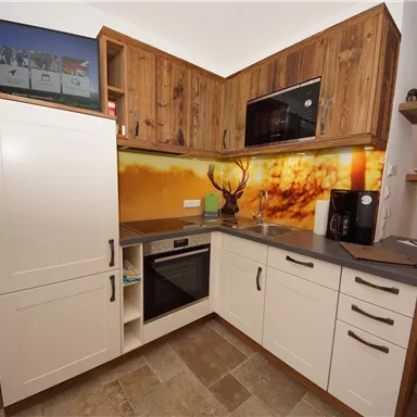 A modern kitchen with wooden surfaces and a sleek counter. The wall is adorned with a vibrant picture and a microwave.