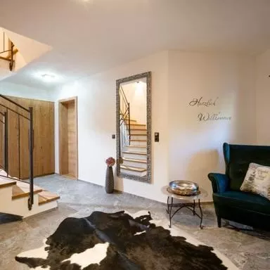 An inviting entrance area with a curved staircase and a large mirror. A cozy armchair and a woven rug give the room a pleasant atmosphere.