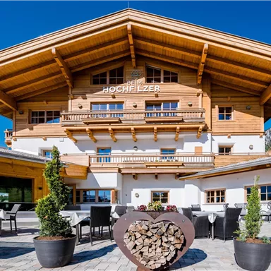 A charming wooden building in alpine style with a large porch.  
Patio furniture and plants invite you to linger.