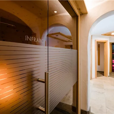 A modern spa area with a glass entrance to an infrared room. The walls are bright and friendly, with cozy lighting in the background.