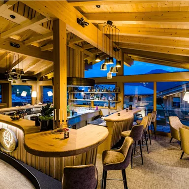 A stylish bar with wooden decor and modern furniture. Large windows provide a view of the surroundings.