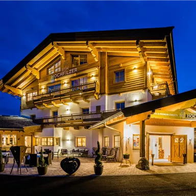 A cozy wooden house with warm light at night. The architecture is traditional and inviting, surrounded by a picturesque landscape.