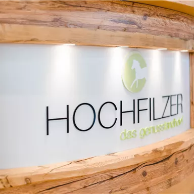 A reception desk made of wood with a modern logo. The inscription "HOCHFILZER" and the slogan "the holistic" are clearly visible.