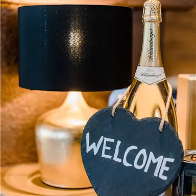 A stylish arrangement with a champagne bottle and a floor lamp. A heart-shaped welcome sign made of slate adds an inviting touch to the scene.