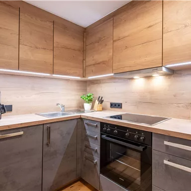 A modern kitchen with wood surfaces and stainless steel appliances. There is a kettle, a stove, and a bottle of wine on the countertop.