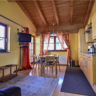 A cozy apartment with wooden details and yellow walls. It has a kitchen, a dining area, and large windows with red curtains.
