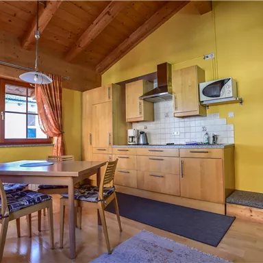 A cozy kitchen with wooden furniture and a dining area. The walls are painted yellow, and large windows provide plenty of daylight.