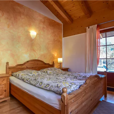 A cozy bedroom with a wooden bed and colorful walls. Next to the bed are two nightstands with lamps, and a large door leads outside.