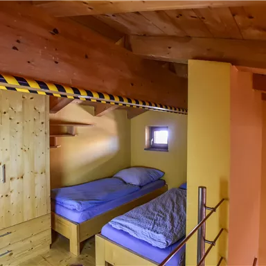 A cozy bedroom with two single beds and wooden cabinets. The walls are painted in warm colors, and there is a small window.