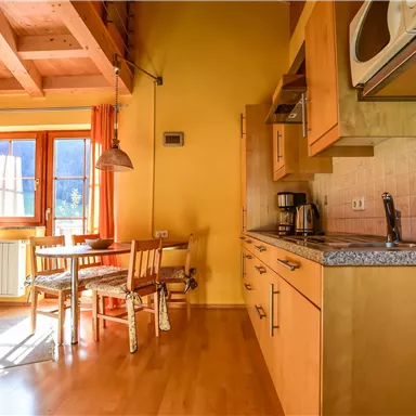 A bright kitchenette with wooden furniture, a table, and chairs. The windows let in plenty of daylight and create a cozy atmosphere.